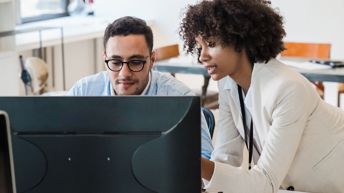 Two colleagues reviewing performance figures on a monitor.